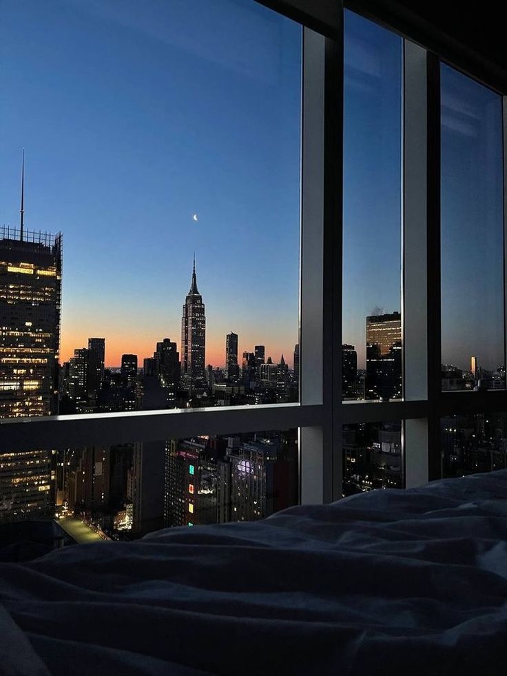 a bed sitting in front of a window next to a cityscape at night