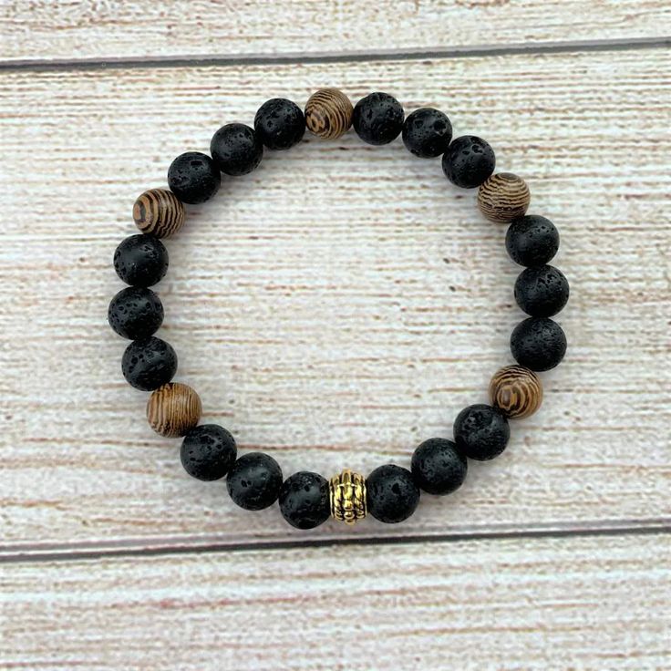 Mens Black Lava and Wood Beaded Bracelet Mens Black Lava and Wood Beaded Bracelet Casual and cool, this black lava and wood beaded bracelet is perfect for the modern man. The 8mm black lava beads are accented with brown wood grain beads and a center gold bead, creating a look that's both stylish and relaxed. The stretch bracelet design makes it easy to put on and take off, making it a great choice for any day or night out. Due to the many variations in monitors and browsers, color may appear different on different monitors Mens Black Lava and Wood Beaded Bracelet   Mens Black Lava and Wood Beaded Bracelet Casual and cool, this black lava and wood beaded bracelet is perfect for the modern man. The 8mm black lava beads are accented with brown wood grain beads and a center gold bead, creating Mens Bracelet Diy, Wooden Beaded Bracelets, Lava Bead Bracelet, Lava Stone Bracelet, Wood Bead Bracelet, Wooden Bracelet, Diy Bracelet Designs, Lava Beads, Wood Bracelet