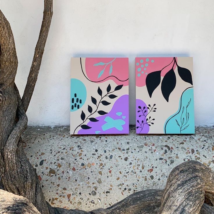 two paintings are sitting next to each other on the ground near a tree and some rocks