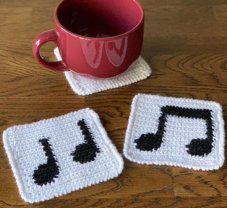 two crocheted coasters with black and white music notes on them next to a cup of coffee