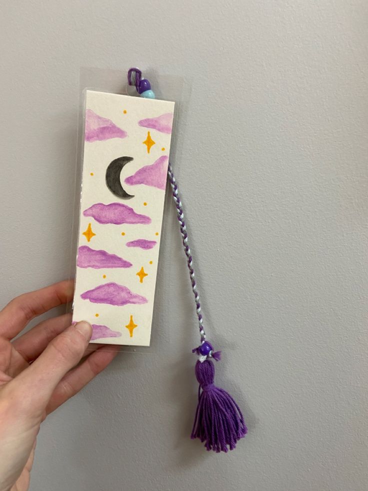 a hand holding a bookmark with a purple tassel hanging from it's side