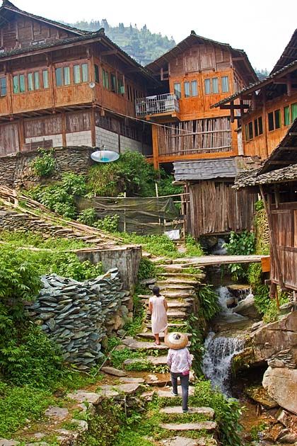 a woman walking up some steps in front of wooden buildings with water running down them