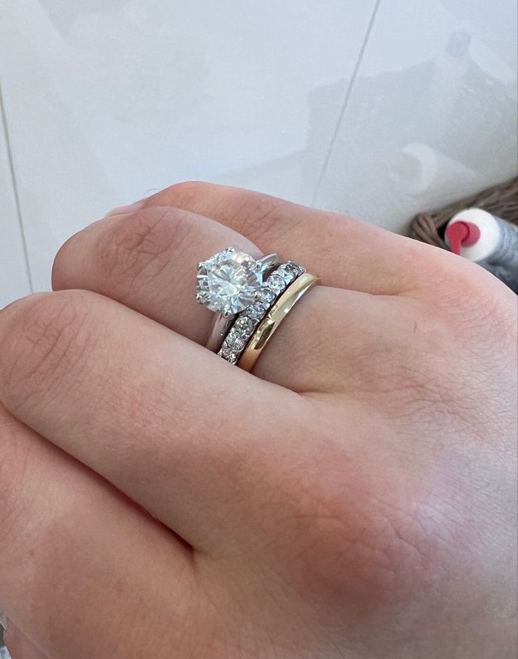 a woman's hand with two wedding rings on top of her finger and an engagement ring in the middle