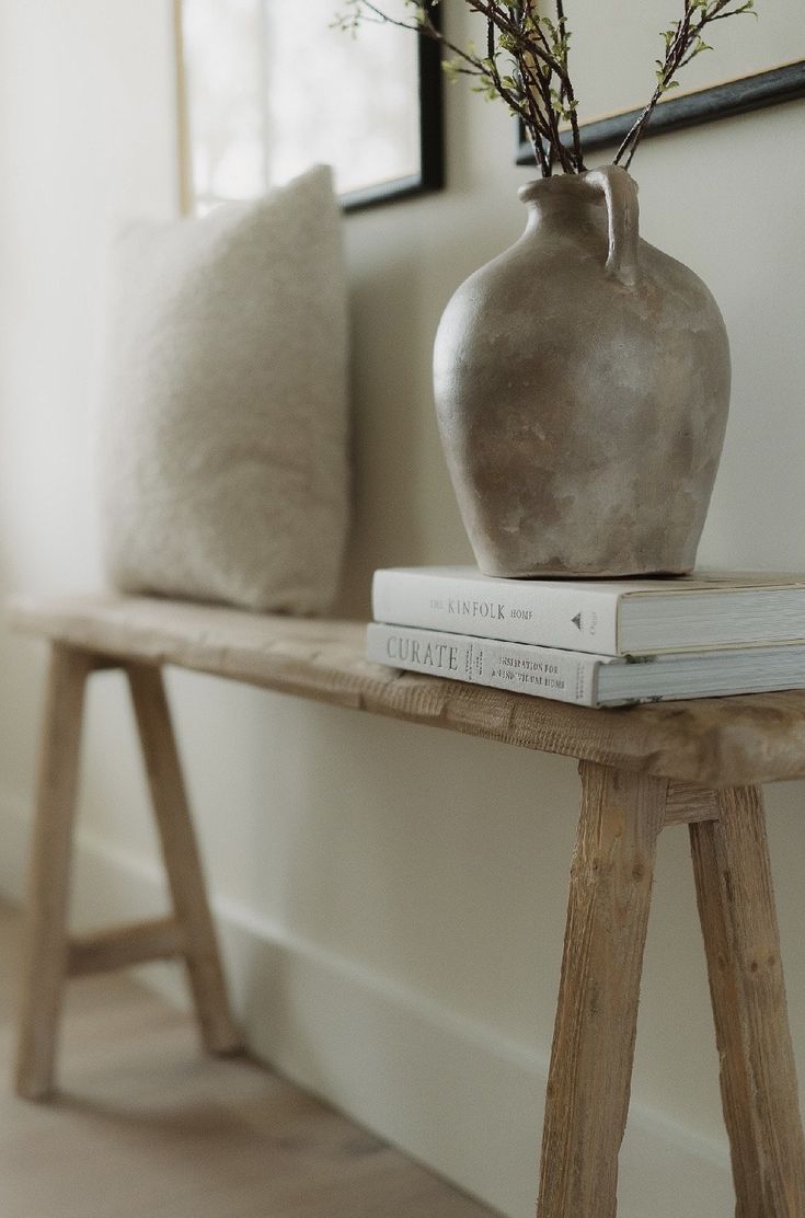 a white vase sitting on top of a wooden table next to two books and a plant