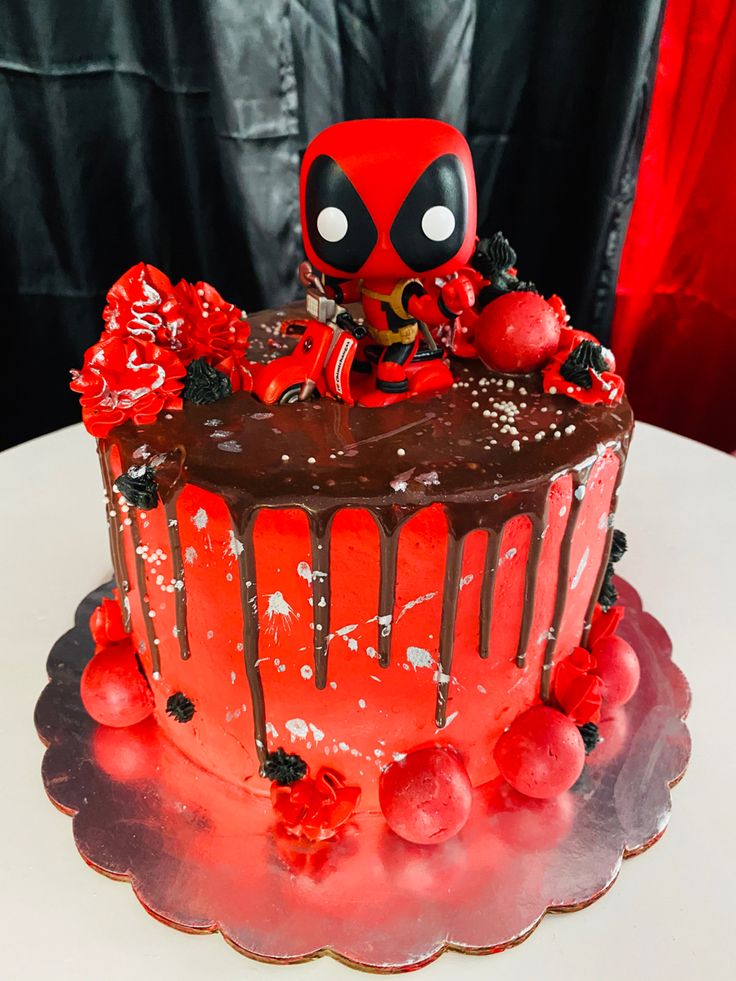 a deadpool cake on a table with red decorations and chocolate frosting that looks like it's dripping from the top