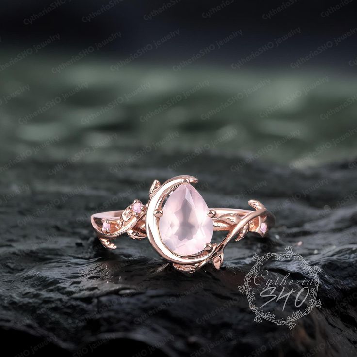 a rose quartz ring sitting on top of a black rock with water droplets around it