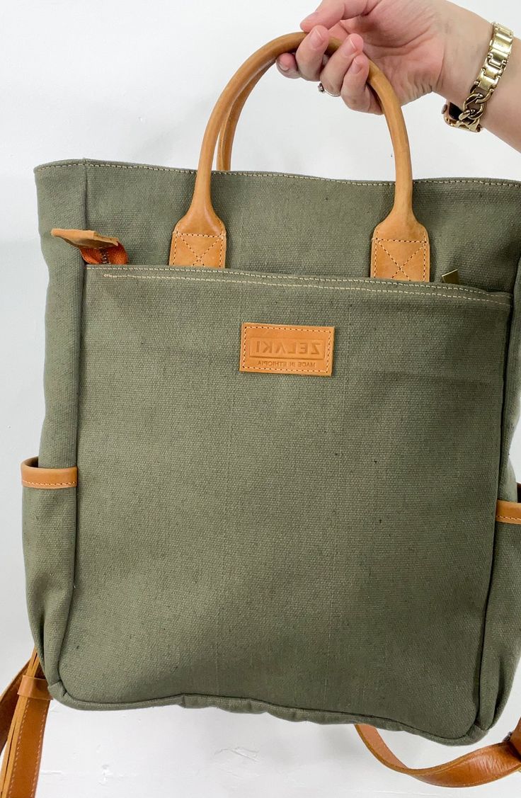 Zelaki Leather Co Canvas Backpack in Olive The Canvas Backpack is a durable and gender-neutral bag that can serve many purposes. With its sturdy design, it can withstand daily wear and tear, making it a reliable choice for those on the go. Details: -Ethically & sustainably made in Ethiopia-Canvas & full-grain leather-Canvas interior-One outside zipping pocket (12"x12") -Zipper closure -Two cupholders -One interior compartment (13"x12")-Adjustable straps-15"H x 12"W x 4"D Canvas Backpack With Top Carry Handle For Daily Use, Functional Khaki Bags For Daily Use, Daily Use Backpack With Top Carry Handle, Travel Bag With Top Carry Handle For Daily Use, Everyday Large Capacity Travel Backpack, Large Capacity Everyday Travel Backpack, Daily Use Travel Bag With Top Carry Handle, Standard Backpack Travel Bag For Daily Use, Large Capacity Laptop Backpack For Everyday Use