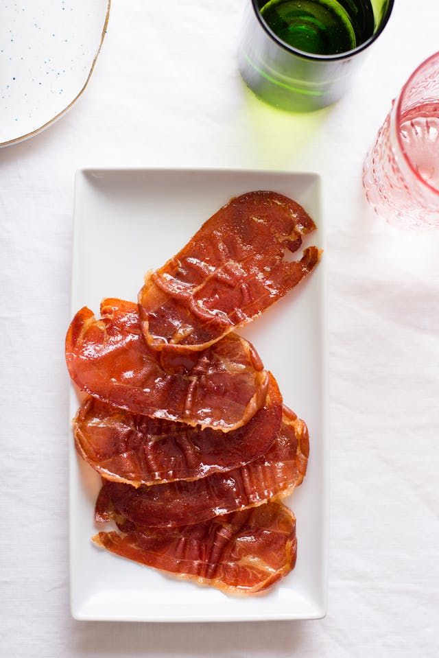 slices of bacon on a white plate next to a glass of water and a green drink