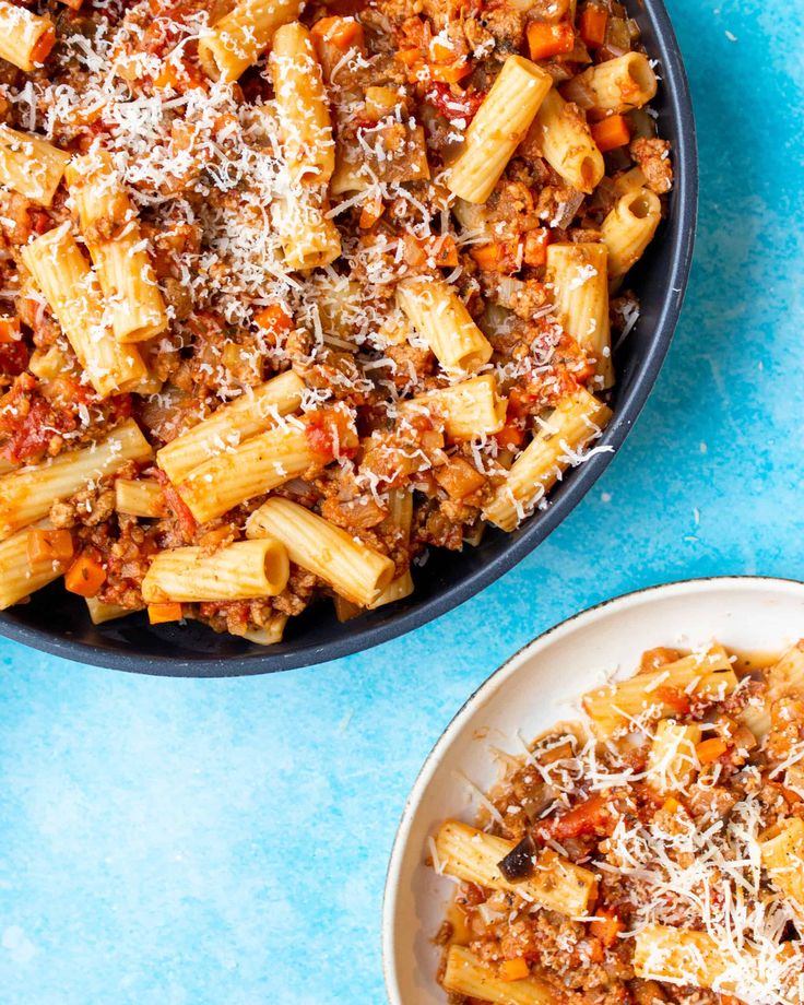 two plates of pasta with meat and parmesan cheese on the top, next to a bowl of sauce