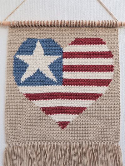 a wall hanging with an american flag heart and star on the front, made out of yarn