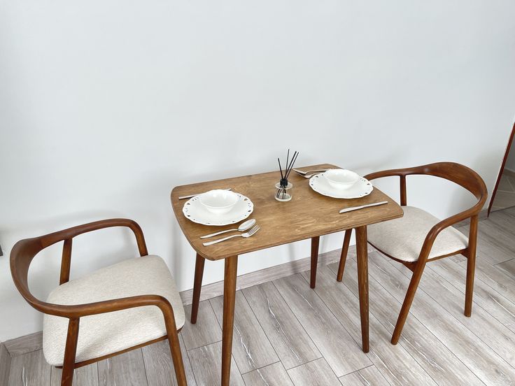 two chairs and a table with plates on it in front of a white painted wall