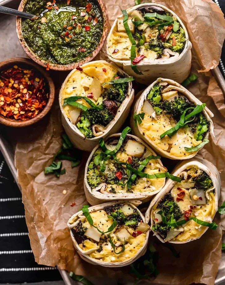 several burritos with broccoli, cheese and other toppings on a tray