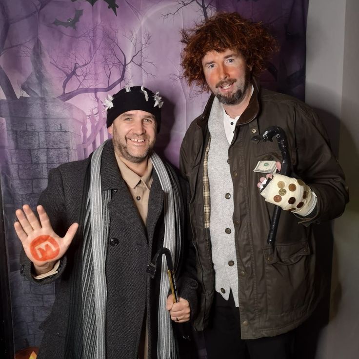 two men standing next to each other in front of a wall with halloween decorations on it