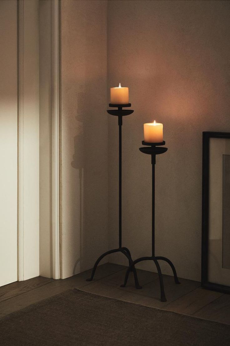 two candles sitting on top of a metal stand next to a mirror and framed photograph