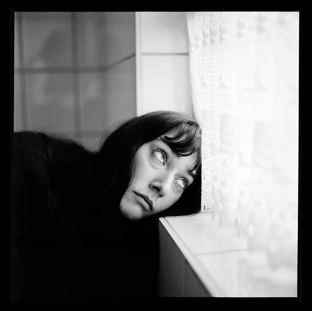 a black and white photo of a woman leaning against a wall with her head on the window sill