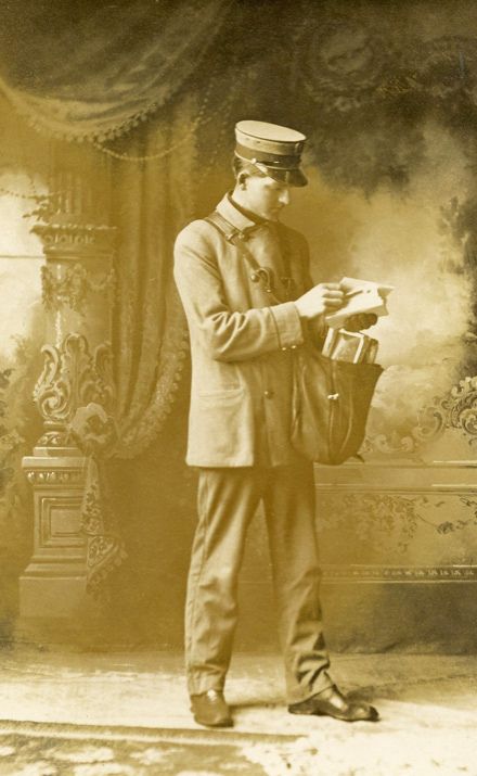 an old photo of a man in uniform holding a bag and looking at something on the ground