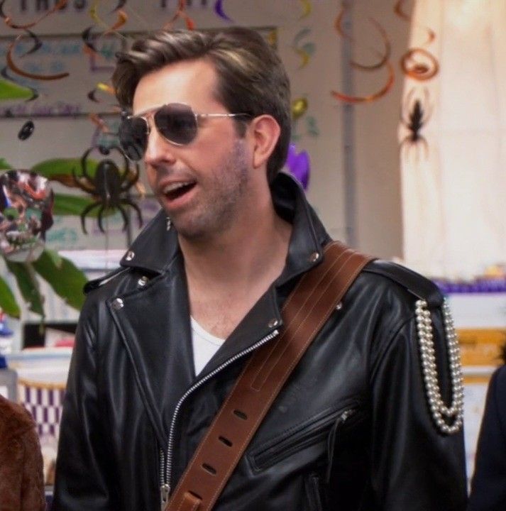 a man in sunglasses and a leather jacket with a guitar strap around his neck is talking to someone