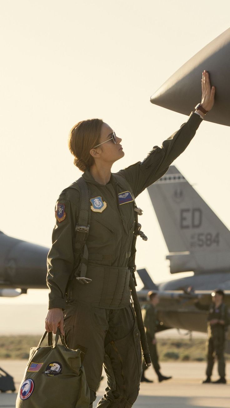 a woman in an air force pilot's uniform is holding up a large object