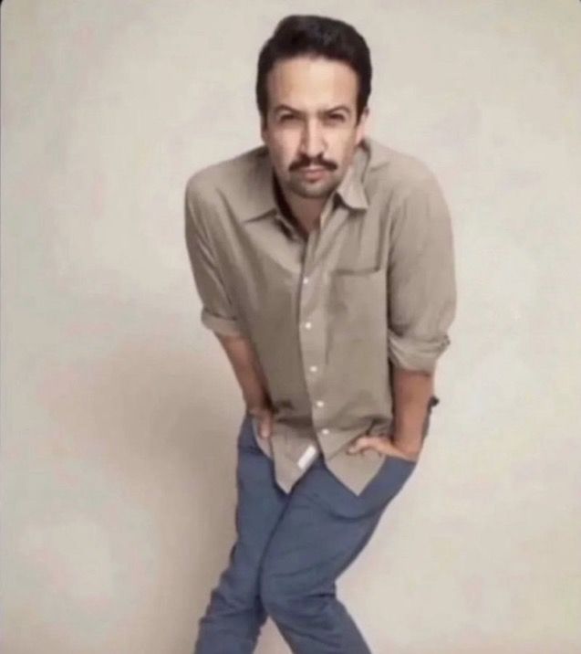 a man with his hands on his hips posing for the camera while wearing blue pants and a button up shirt