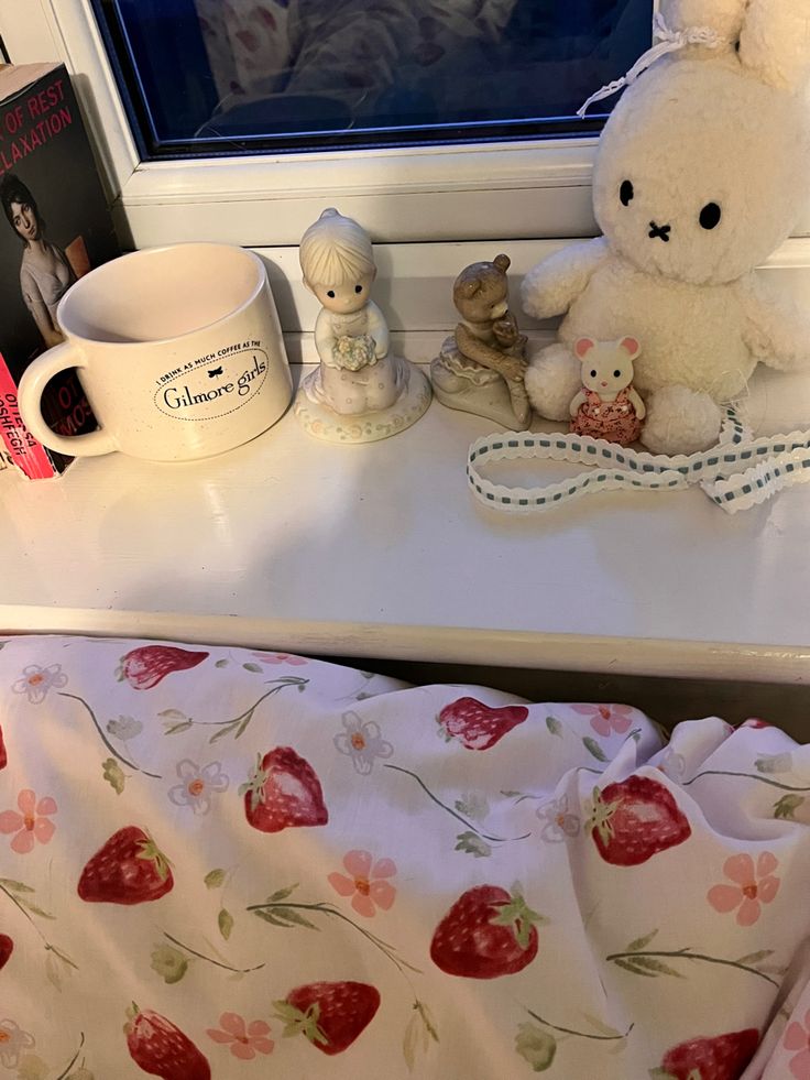 a white teddy bear sitting on top of a window sill next to a cup