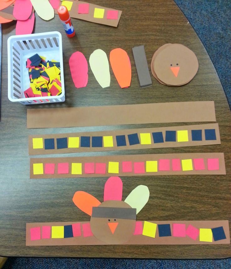 a wooden table topped with paper cut out of turkeys and strips of construction paper