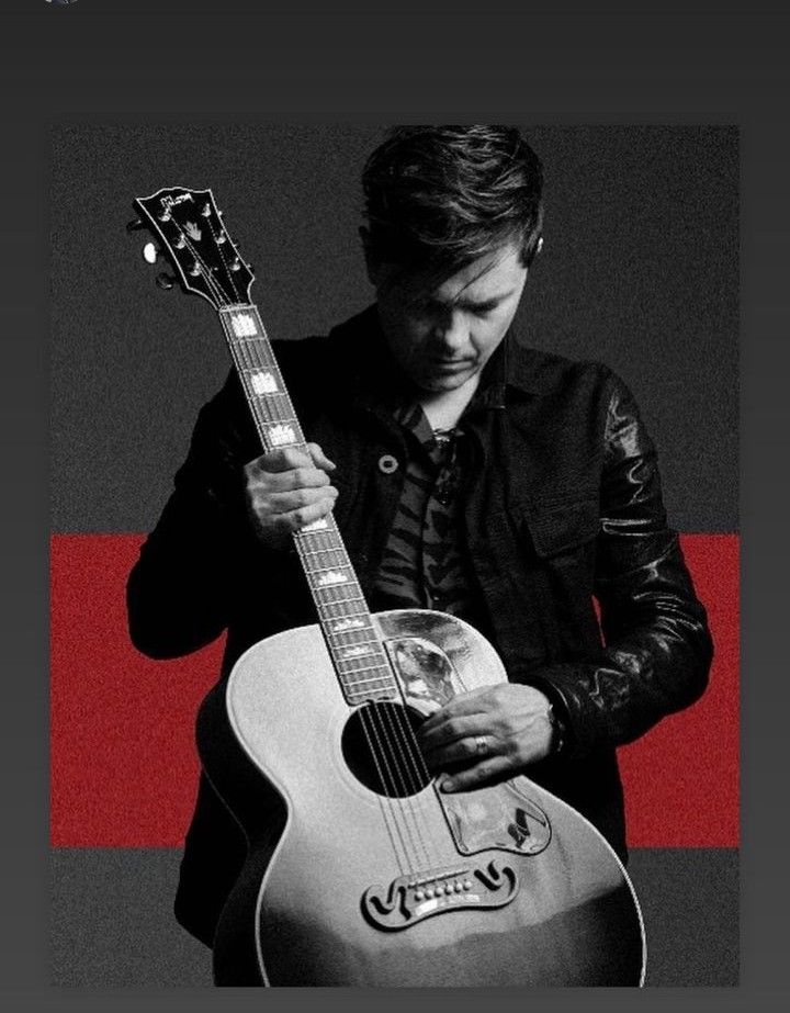 a man holding a guitar in front of a red and black background