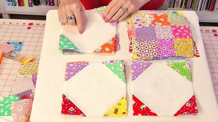 a woman is making a quilt on a table with scissors and paper pieces in front of her