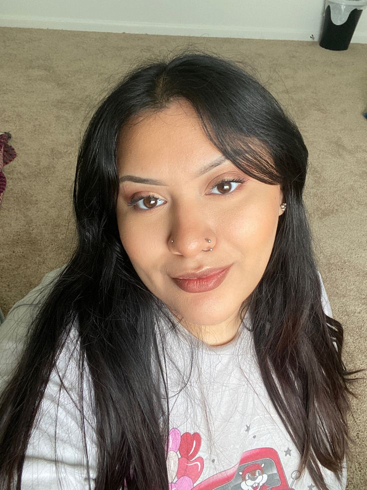 a woman with long black hair sitting on the floor and looking at the camera while holding a cell phone in her hand