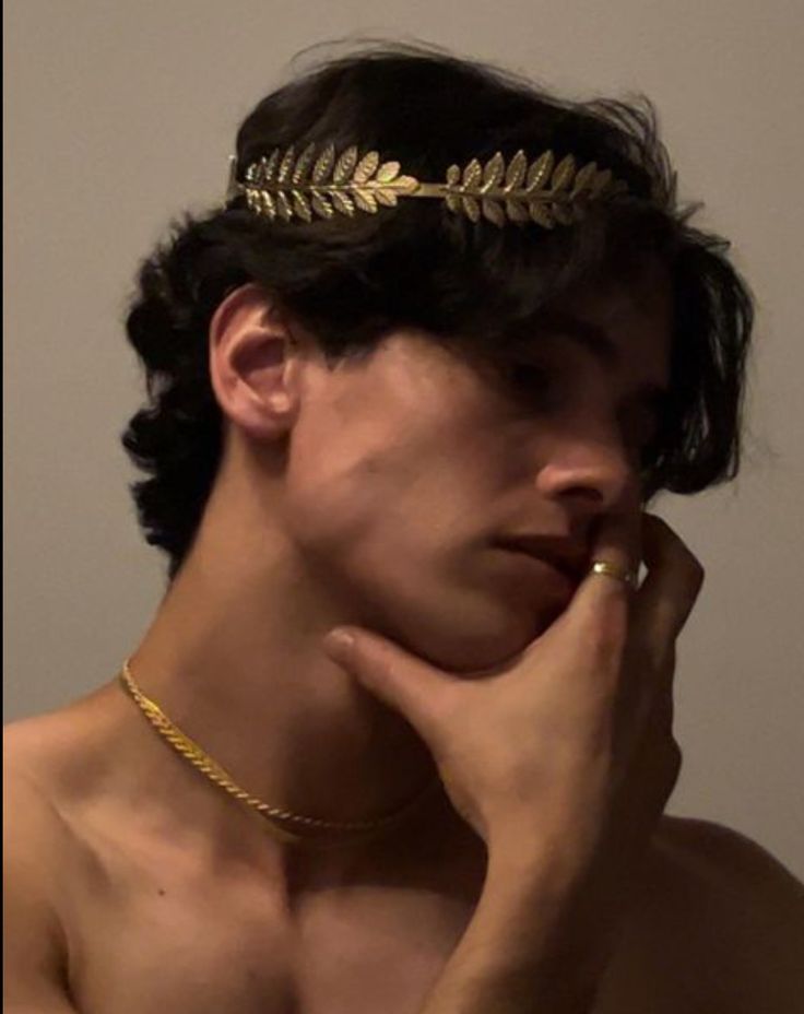 a shirtless man wearing a gold leaf headband on top of his neck and hand under his chin