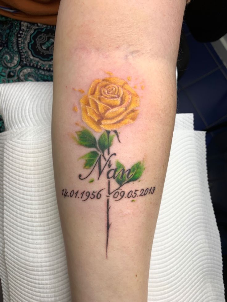 a yellow rose tattoo on the arm with words written below it and a green leaf