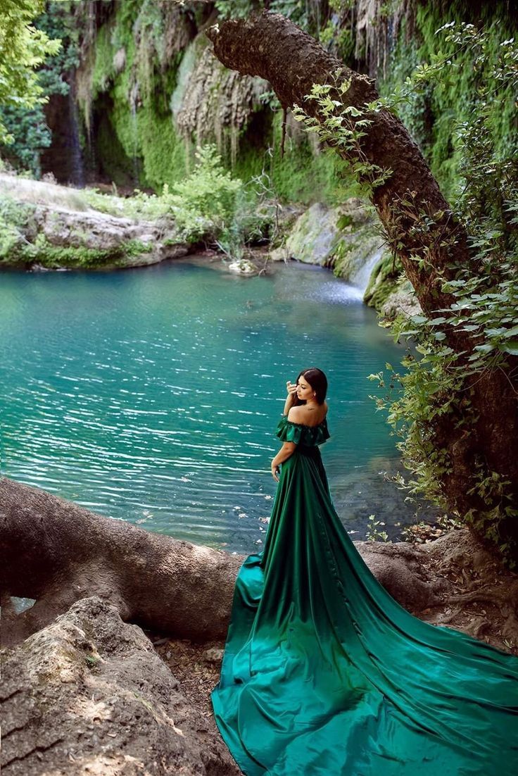 a woman in a long green dress standing by a river