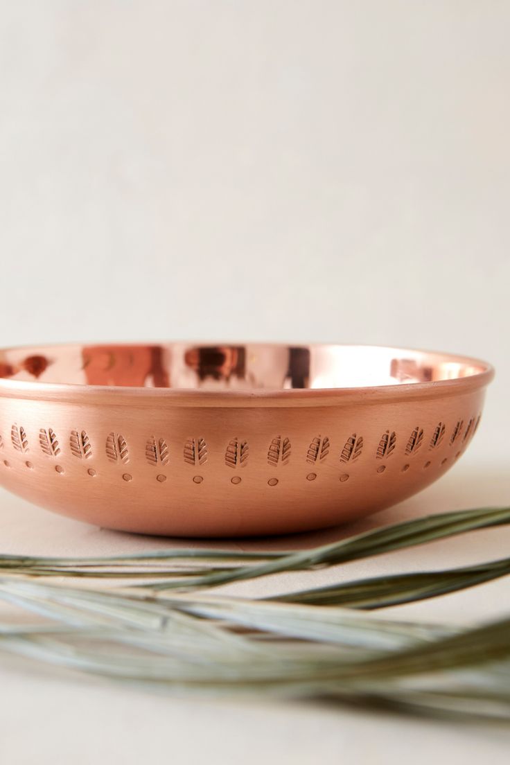 a large metal bowl sitting on top of a white table next to some green leaves