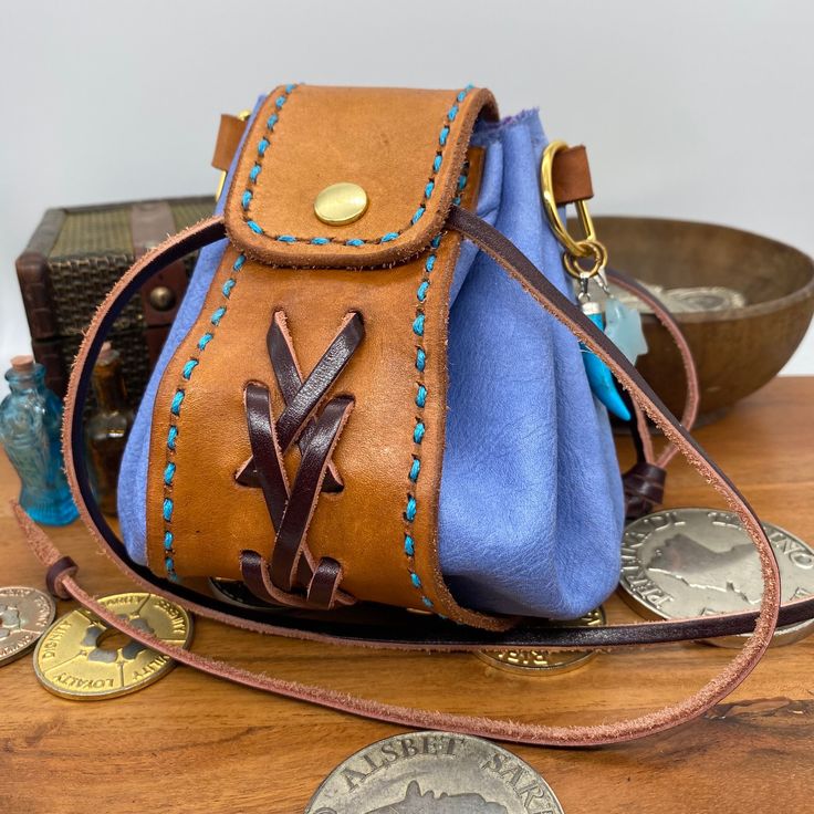 Looking for a stylish storage solution for your dice? Coin pouch for your Larp costume or D&D cosplay? This handcrafted leather bag might just be for you. Warm Tan hand stained vegtan leather main band with dark brown braided detail, and pale blue soft leather circle body section.  Brass coloured metalwork including a press popper to the front, eyelets on all the drawstring holes, 2 D-rings, and 2 semi precious stone charms. Size: approximately 130mm tall and wide Images show the bag empty and r Blue Leather Pouch For Daily Use, Adjustable Leather Bag Gift, Adjustable Leather Pouch Bag, Leather Pouch With Case Included For Gift, Adjustable Leather Bags For Personal Use, Gift Leather Pouch With Case Included, Blue Leather Bag For Personal Use, Leather Pouch With Case For Everyday Use, Handmade Leather Pouch For Everyday Use