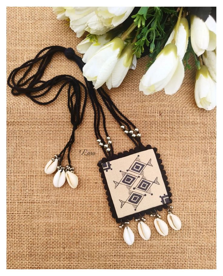 a necklace with shells and beads hanging from it's end on a table next to flowers