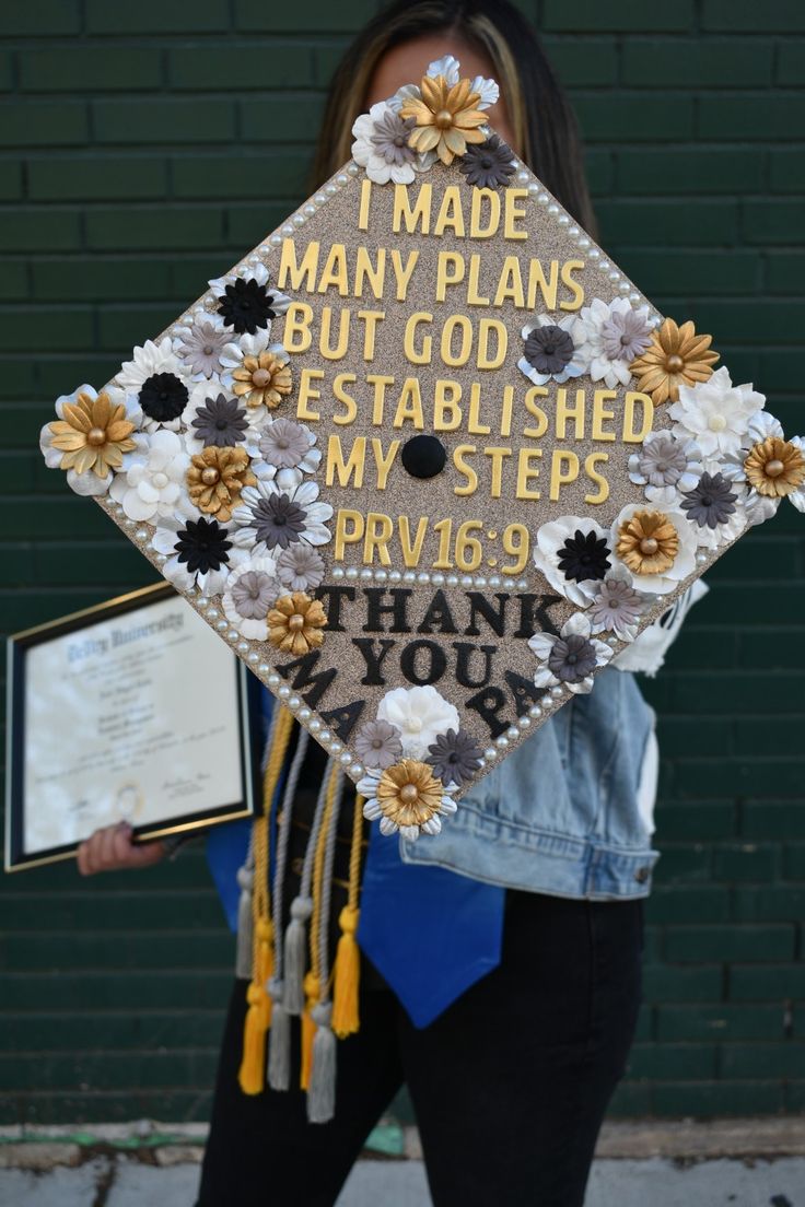 a woman holding a decorated graduation cap with words on it and flowers in the center