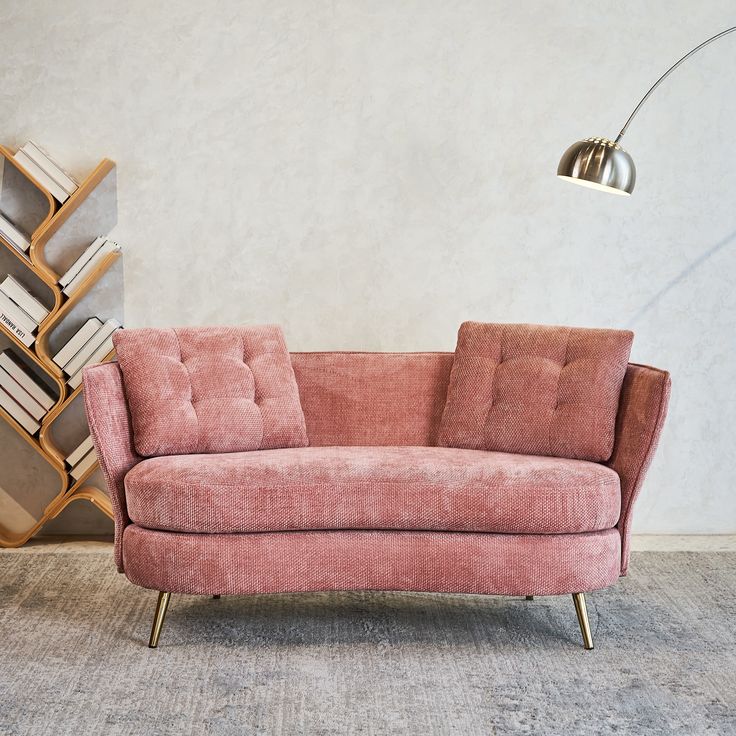 a pink couch sitting next to a tall book shelf with books on top of it