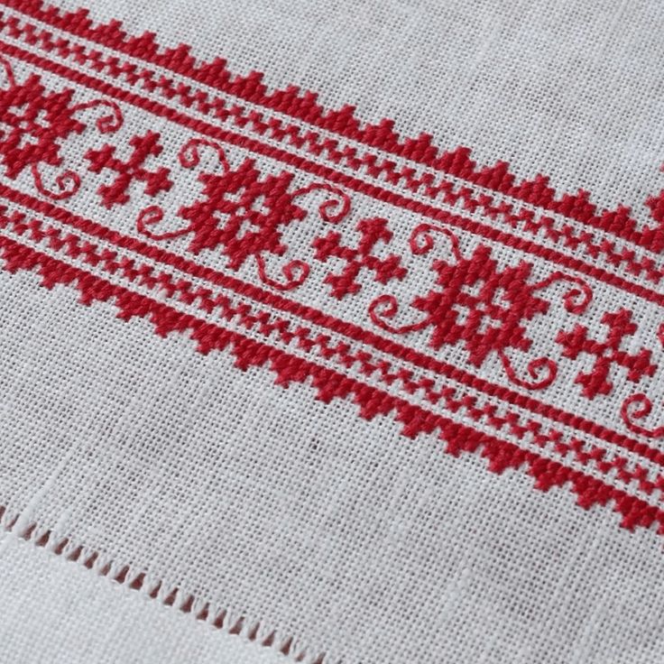 a red and white table cloth with an embroidered design on the edge, sitting next to a pair of scissors