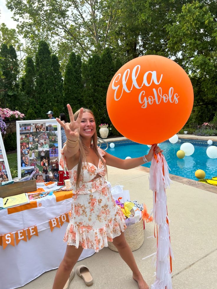 a woman holding up an orange balloon in front of a pool