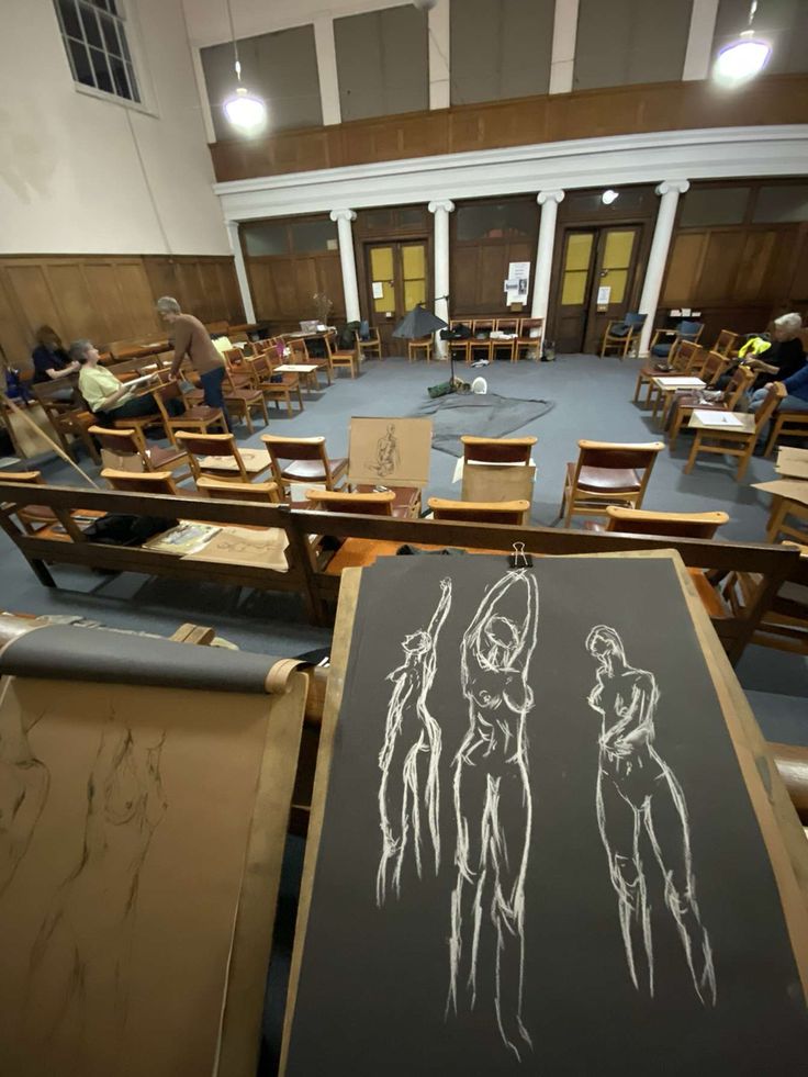 an empty room filled with lots of wooden chairs and paintings on easels in front of them