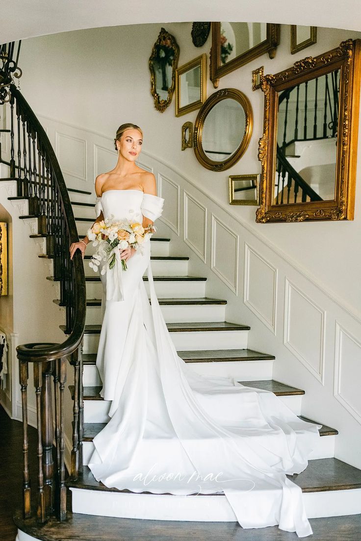 a woman in a white dress is standing on the stairs with her bouquet and looking at the camera