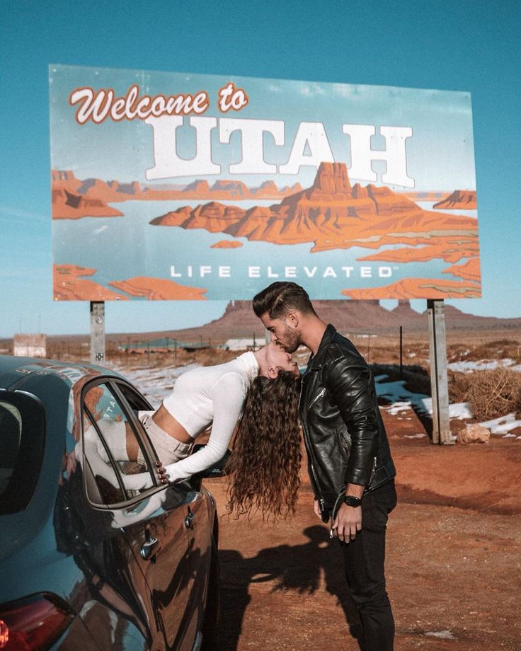 a man and woman kissing in front of a sign that reads welcome to utah life elevated