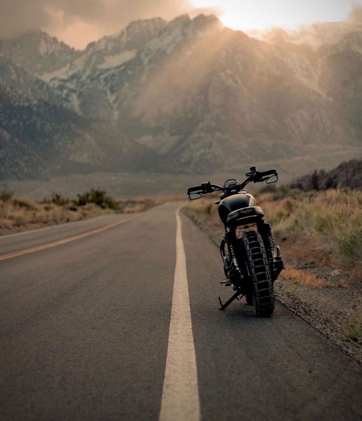 the motorcycle is parked on the side of the road with mountains in the back ground