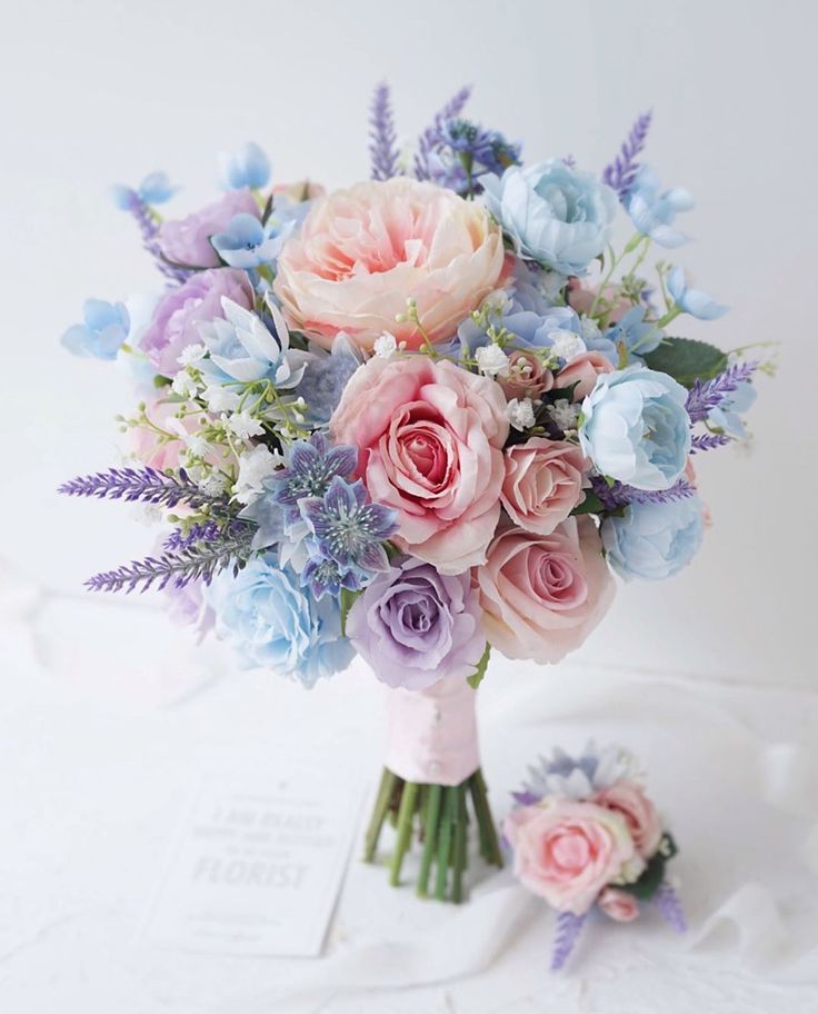 a bouquet of pink and blue flowers on a white tablecloth with a card in the background