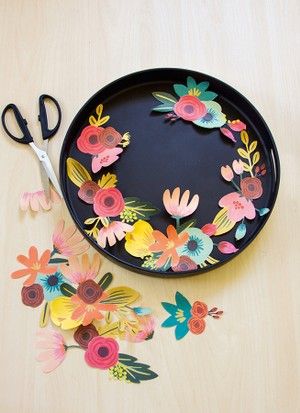 scissors and paper flowers on a black plate next to some cut out pieces of paper