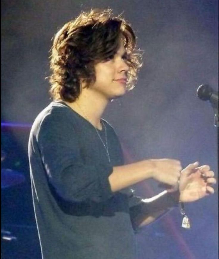 a young man standing in front of a microphone on stage with his hands folded out