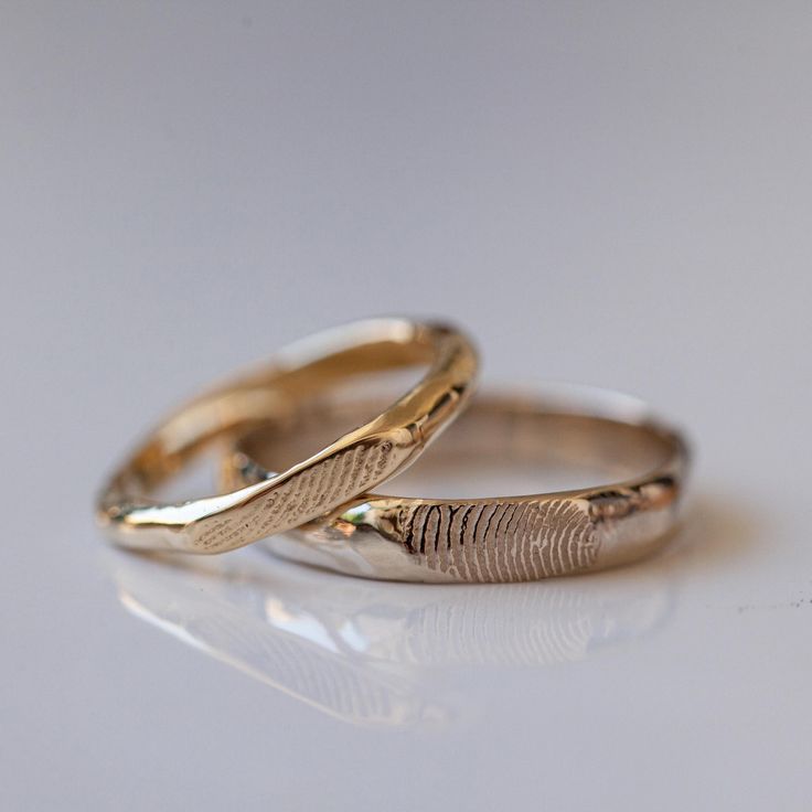 two gold wedding rings with fingerprints on them sitting on a white table top