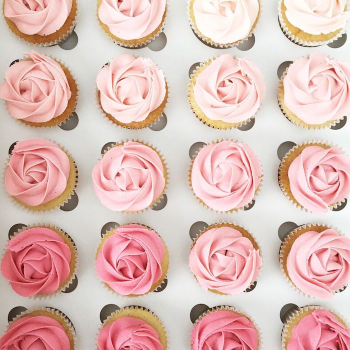 cupcakes with pink frosting are arranged in rows on a white surface,