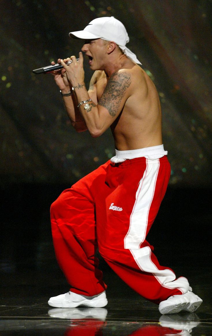 a shirtless man in red and white pants holding a microphone while standing on stage