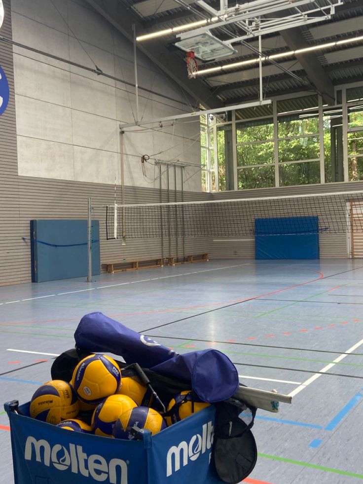 a blue box filled with yellow balls on top of a tennis court in an indoor gym