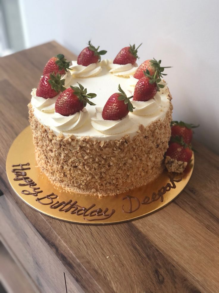 a cake with strawberries on top sitting on a wooden table next to a wall